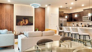 A modern living room with a sofa, a glass coffee table, and a dining area with chairs. - Family-friendly Townhouse w/ Private Pool & Game Room (Clermont)