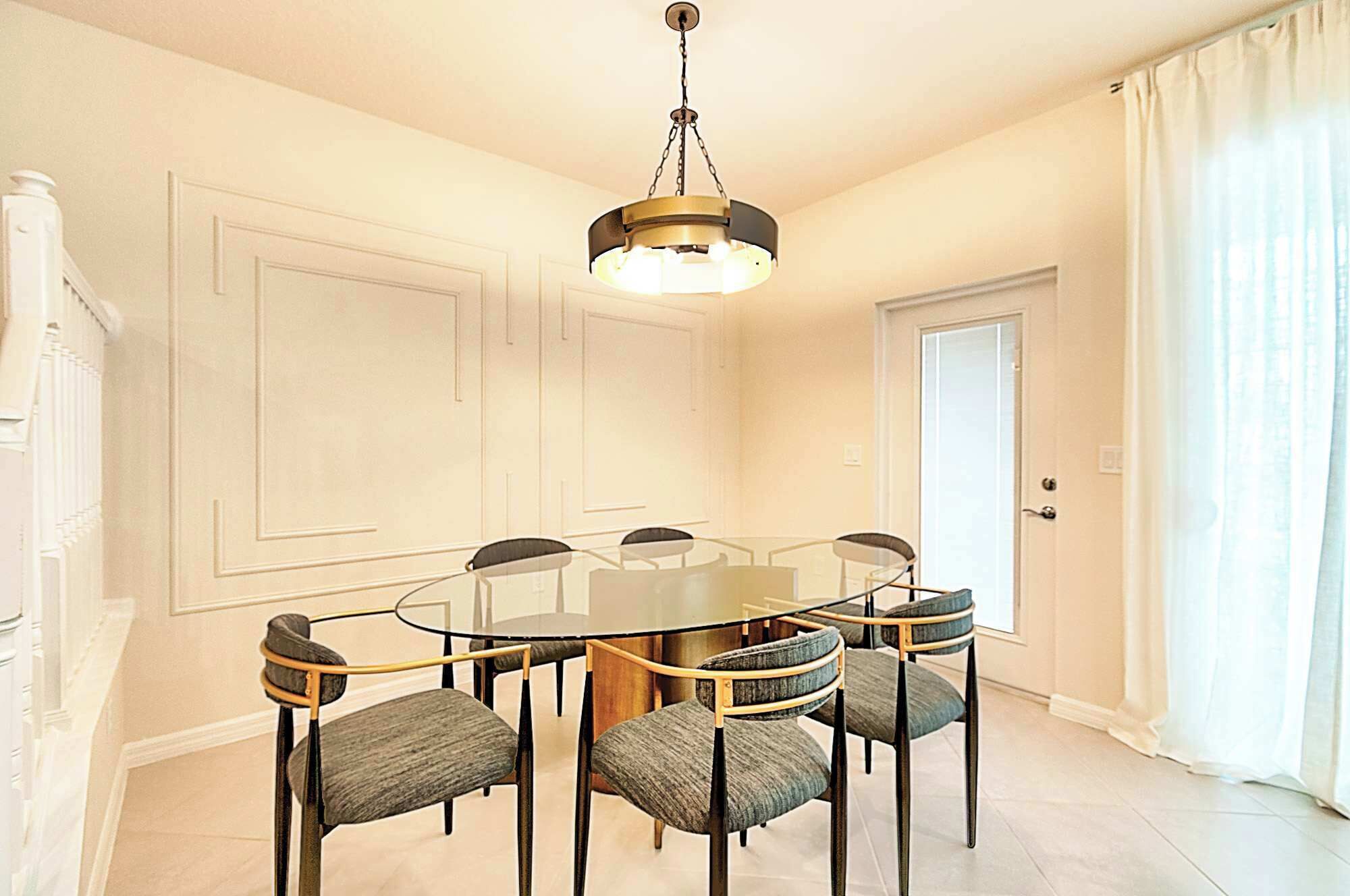 Ein Esszimmer mit einem runden Tisch, sechs Stühlen, einer Chandelier und einer mit Vorhängen versehenen Tür.