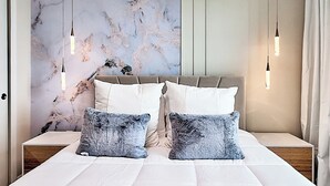 A bedroom with a marble wall, a bed with white bedding, two grey pillows, and pendant lights. - Family-friendly Townhouse w/ Private Pool & Game Room (Clermont)