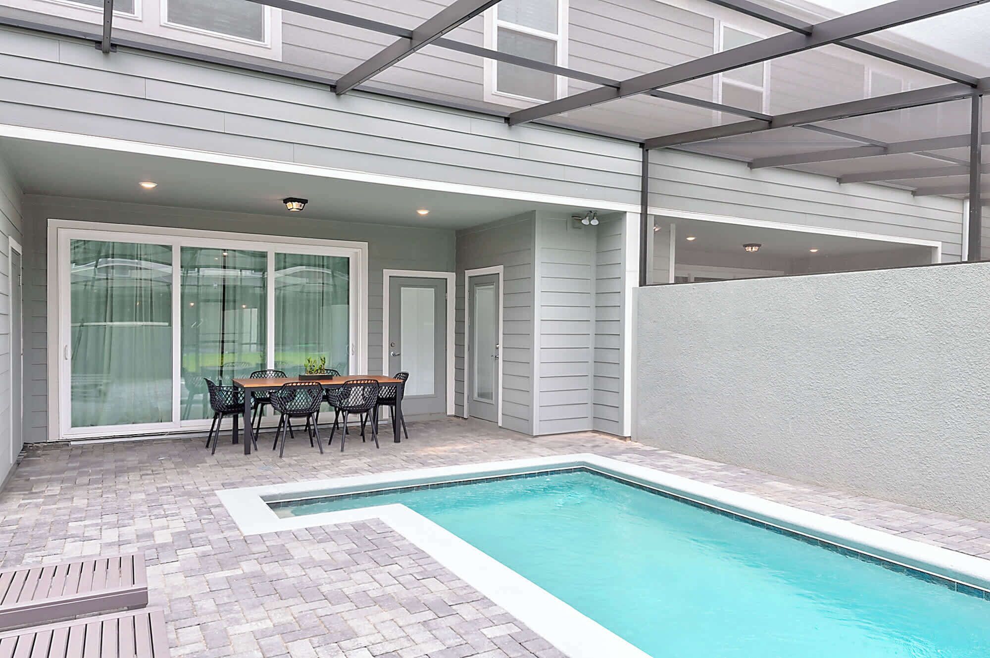 Un patio couvert avec une piscine, une table et des chaises, et une porte vitrée donnant sur un garage.