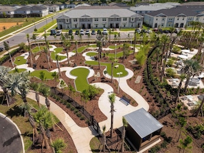 An aerial view of a residential area with modern apartment buildings, a winding pathway, and landscaped areas with palm trees.