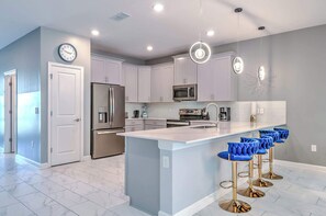 A modern kitchen with a central island, stainless steel appliances, and bar stools. - Family-friendly House With Private Pool & Game Room (Kissimmee)