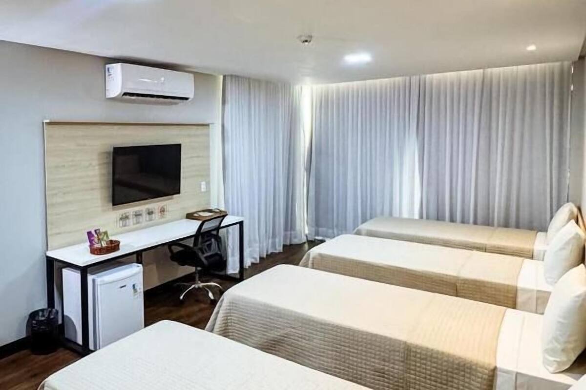 A hotel room with two beds, a desk, a chair, a television, and a window with curtains.