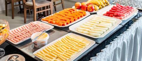 Un bufé con diferentes opciones de comida, como frutas cortadas, verduras y pasta.