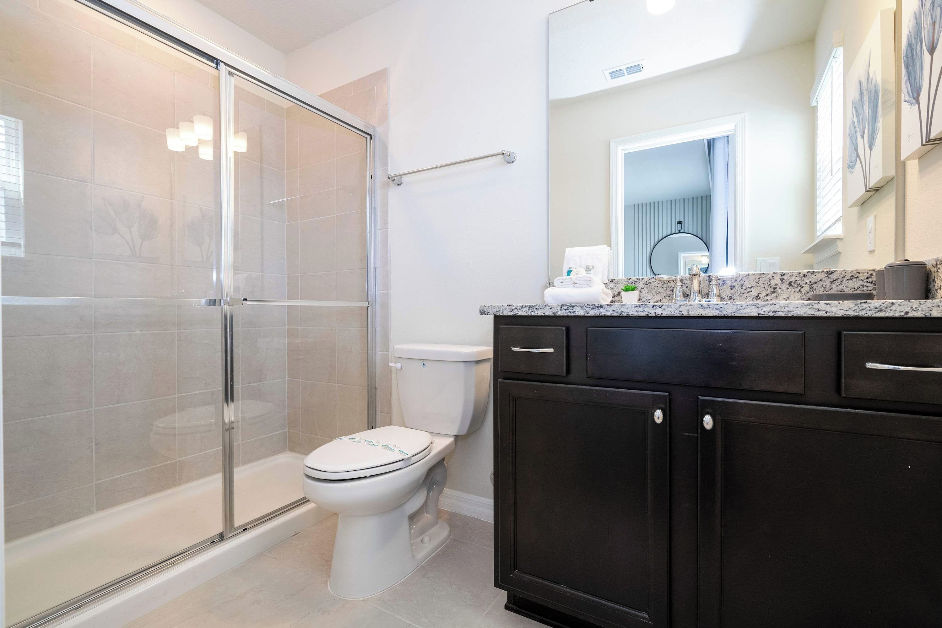 A modern bathroom with a glass-enclosed shower, a white toilet, and dark cabinetry.