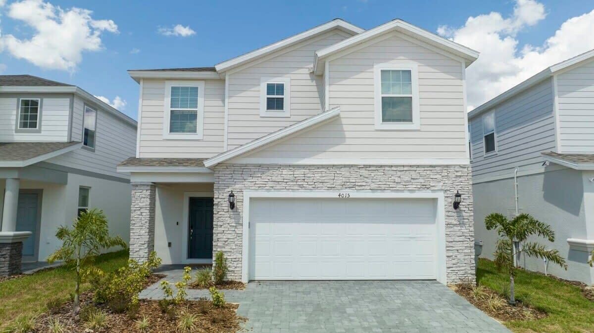 A two-story house with a stone facade, a garage, and a small front yard with plants.