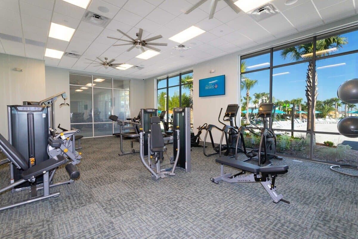 A gym with various exercise equipment, large windows, and a ceiling fan.