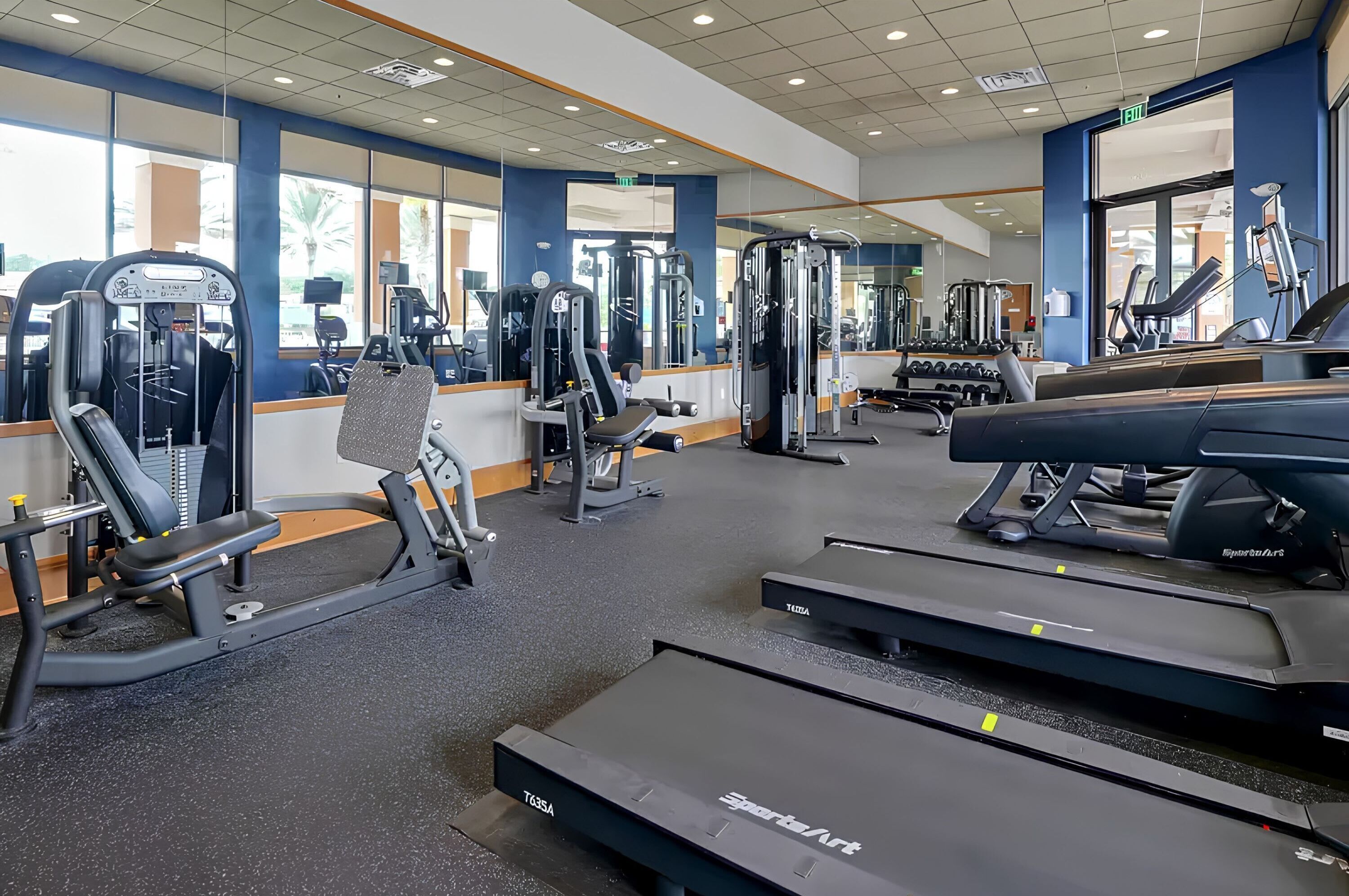Une salle de sport équipée de divers appareils d’exercice, de miroirs et de tapis de course.