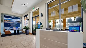 Et receptionsområde med et stort skilt, en receptionistskranke og et siddeområde med stole og et bord.