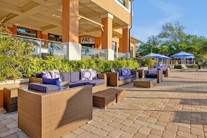 Outdoor seating with wicker furniture and cushions, a covered area with umbrellas, and a building with signage for 'ZAC'S Sports Bar & Grill'. - Modern Family 4BR Townhome Near Disney in Orlando (Kissimmee)