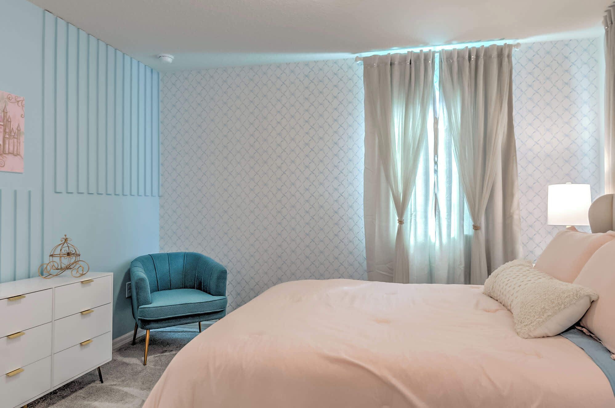 Un dormitorio con cama, una silla, un aparador y una ventana con cortinas.