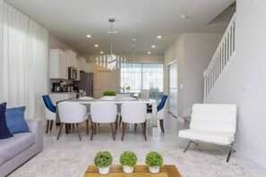 Eine moderne Küche mit weißen Schränken, ein Essbereich mit weißem Tisch und Stühlen, ein weißes Sofa und eine Treppe.
