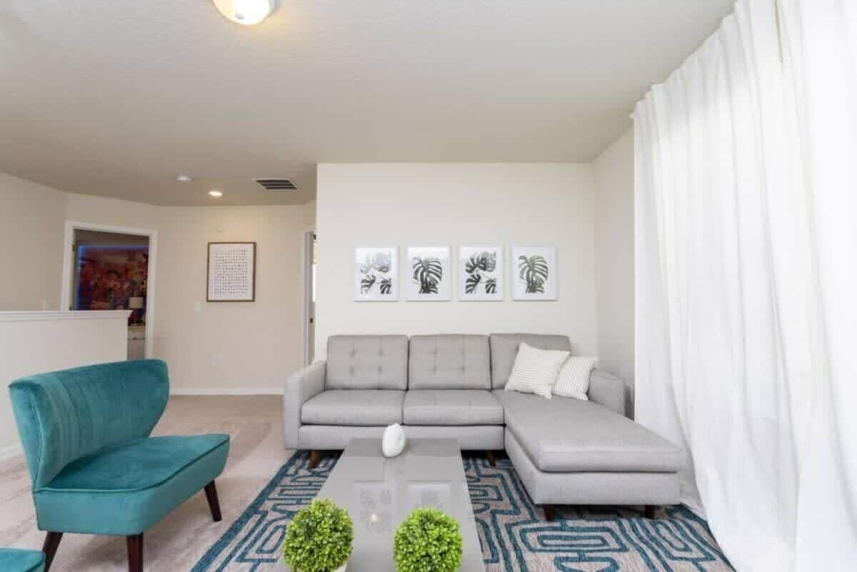 Una sala de estar moderna con un sofá gris, un sillón azul turquesa y un tapete estampado.