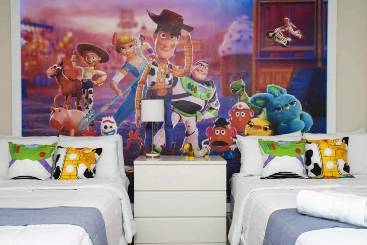 Un dormitorio con dos camas, una mesita de noche y un cartel con personajes animados.