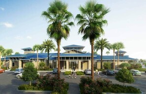 Ein Hotel mit modernem Design, das einen zentralen Eingang, von Palmen gesäumt, einen Parkplatz und einen klaren Himmel zeigt.