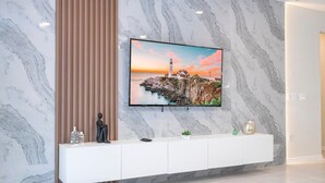 A modern living room with a marble wall, a mounted TV, and a white console with decorative items. - Spacious Family Retreat w/ Pool at Windsor Island (Davenport)