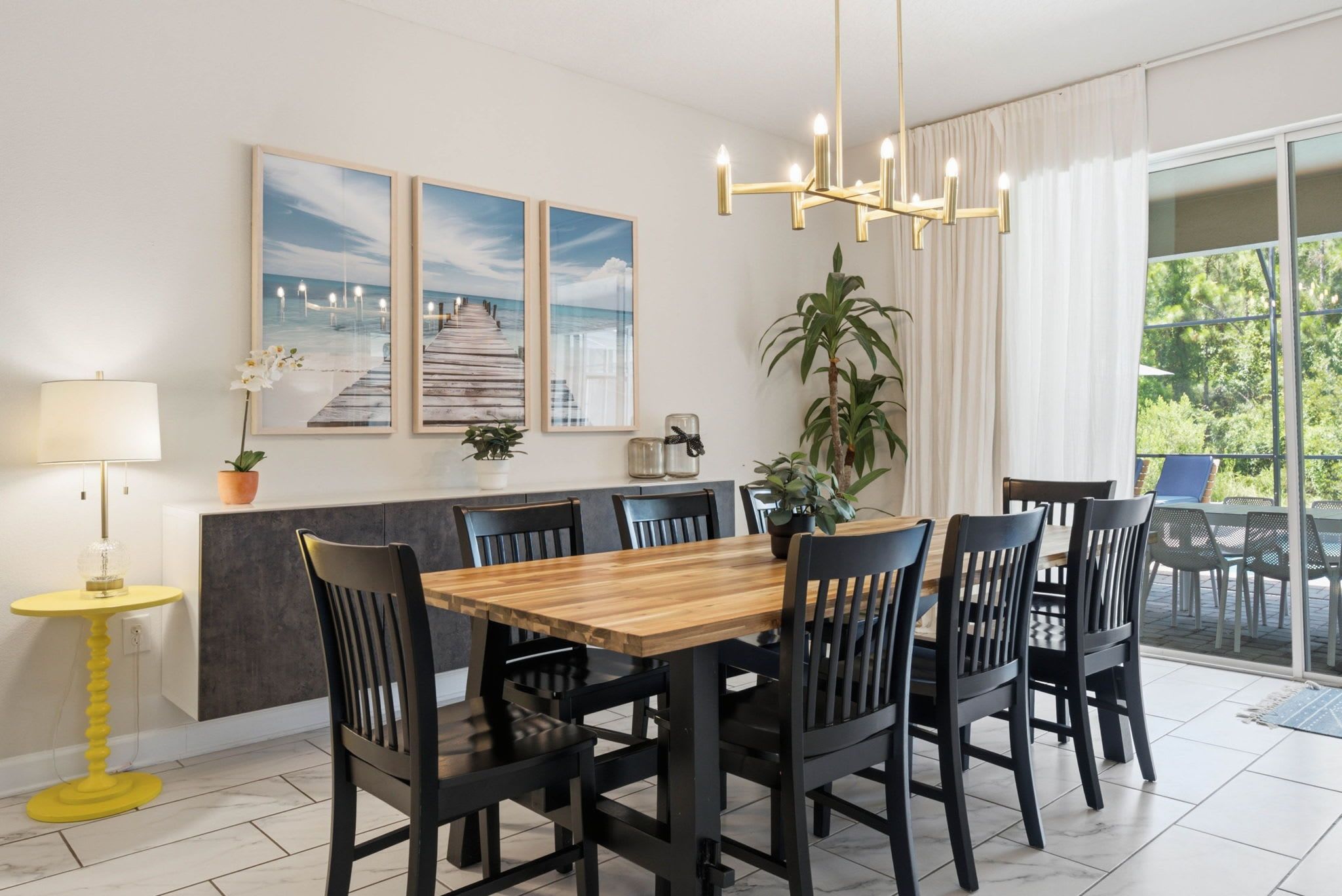 A dining area with a wooden table and black chairs, a yellow lamp, and framed pictures on the wall.