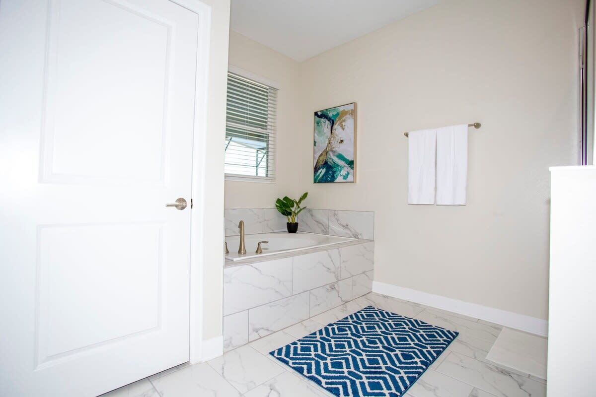 Une salle de bain avec une porte blanche, une baignoire, un lavabo, un porte-serviettes et un tapis bleu à motifs.