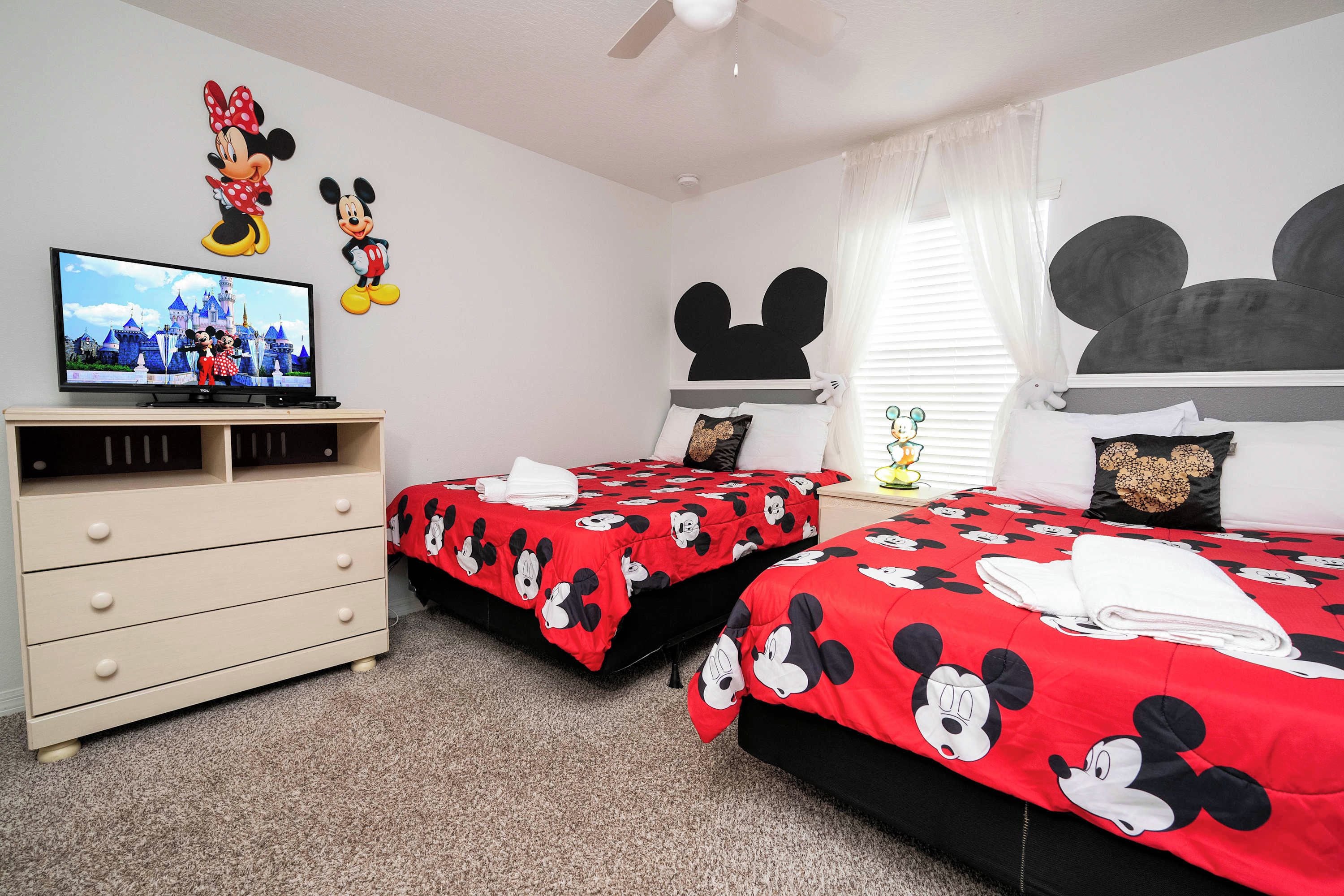 A hotel room with two beds, a TV, and Mickey Mouse decorations.