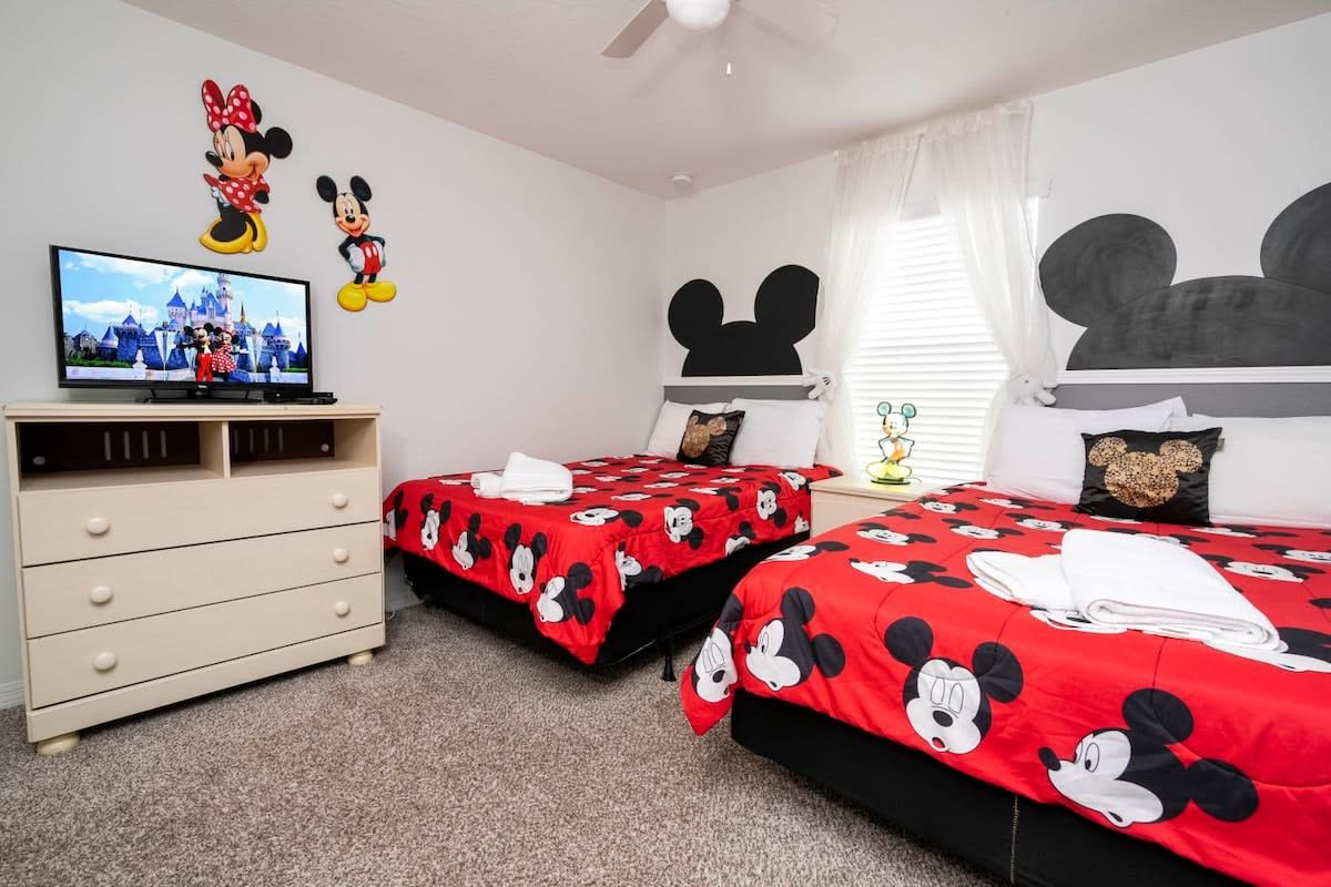 A room with two beds, a TV, and Mickey Mouse decorations.
