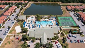 Vista aérea de un complejo turístico con piscina, canchas de tenis y un edificio grande con estacionamiento.