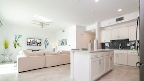 A modern kitchen with white cabinetry, a central island, and a dining area with a sofa. - Themed Family Apartment With Pool Near Disney (Kissimmee)