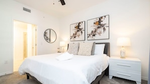 A bedroom with a bed, bedside tables, a mirror, and abstract wall art. - Themed Family Apartment With Pool Near Disney (Kissimmee)