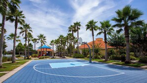 Ein Basketballplatz im Freien, umgeben von Palmen und einem Gebäude mit rotem Dach.