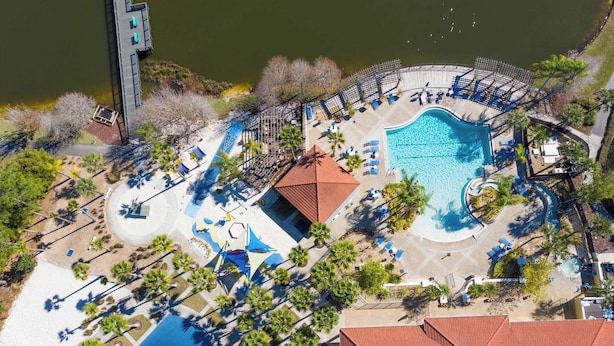 Ein Luftbild eines Resorts mit Swimmingpool, Liegestühlen und Palmen.