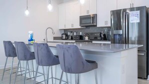 A modern kitchen with white cabinets, stainless steel appliances, and bar stools. - Modern Family Townhouse With Private Pool in Storey Lake (Kissimmee)