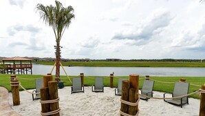 A beach area with chairs and a palm tree, a wooden fence, and a view of a body of water and distant buildings. - Modern Family Townhouse With Private Pool in Storey Lake (Kissimmee)