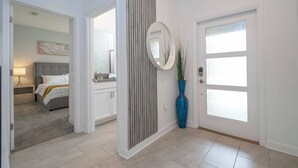 A hallway with a door, a mirror, a blue vase, and a bed in the background. - Modern Family Townhouse With Private Pool in Storey Lake (Kissimmee)