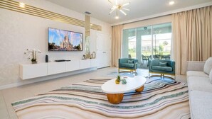A modern living room with a flat-screen TV, a white entertainment unit, a patterned rug, and two teal armchairs. - Luxury Family Home w/ Private Pool & Clubhouse (Davenport)