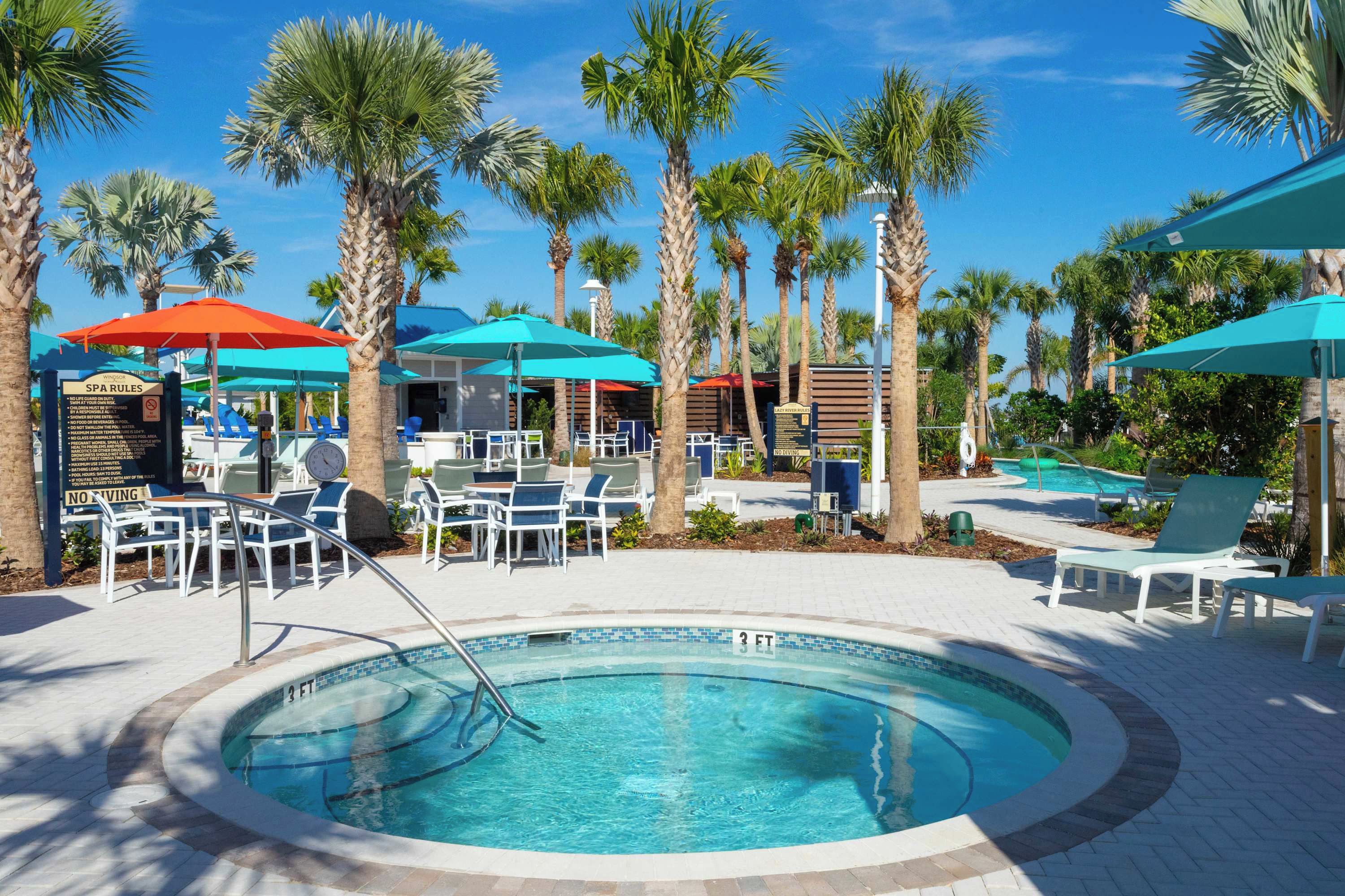 A pool area with lounge chairs, umbrellas, and palm trees.