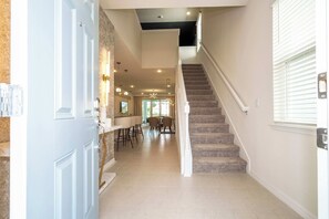 A modern kitchen with a central island, a dining area with chairs, and a staircase leading to an upper floor. - Luxury Family Home w/ Private Pool & Clubhouse (Davenport)