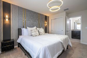 A modern bedroom with a large bed, bedside tables, a wardrobe, and a bathroom visible through an open door. - Luxury Family Home w/ Private Pool & Clubhouse (Davenport)