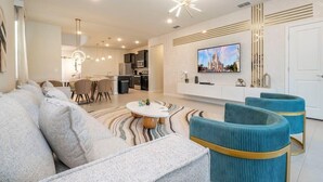 A modern living room with a sofa, ottoman, and a dining area with chairs and a table. - Luxury Family Home w/ Private Pool & Clubhouse (Davenport)