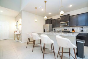 Een moderne keuken met donkere kastjes, roestvrijstalen apparatuur en een bargedeelte met witte barstoelen.