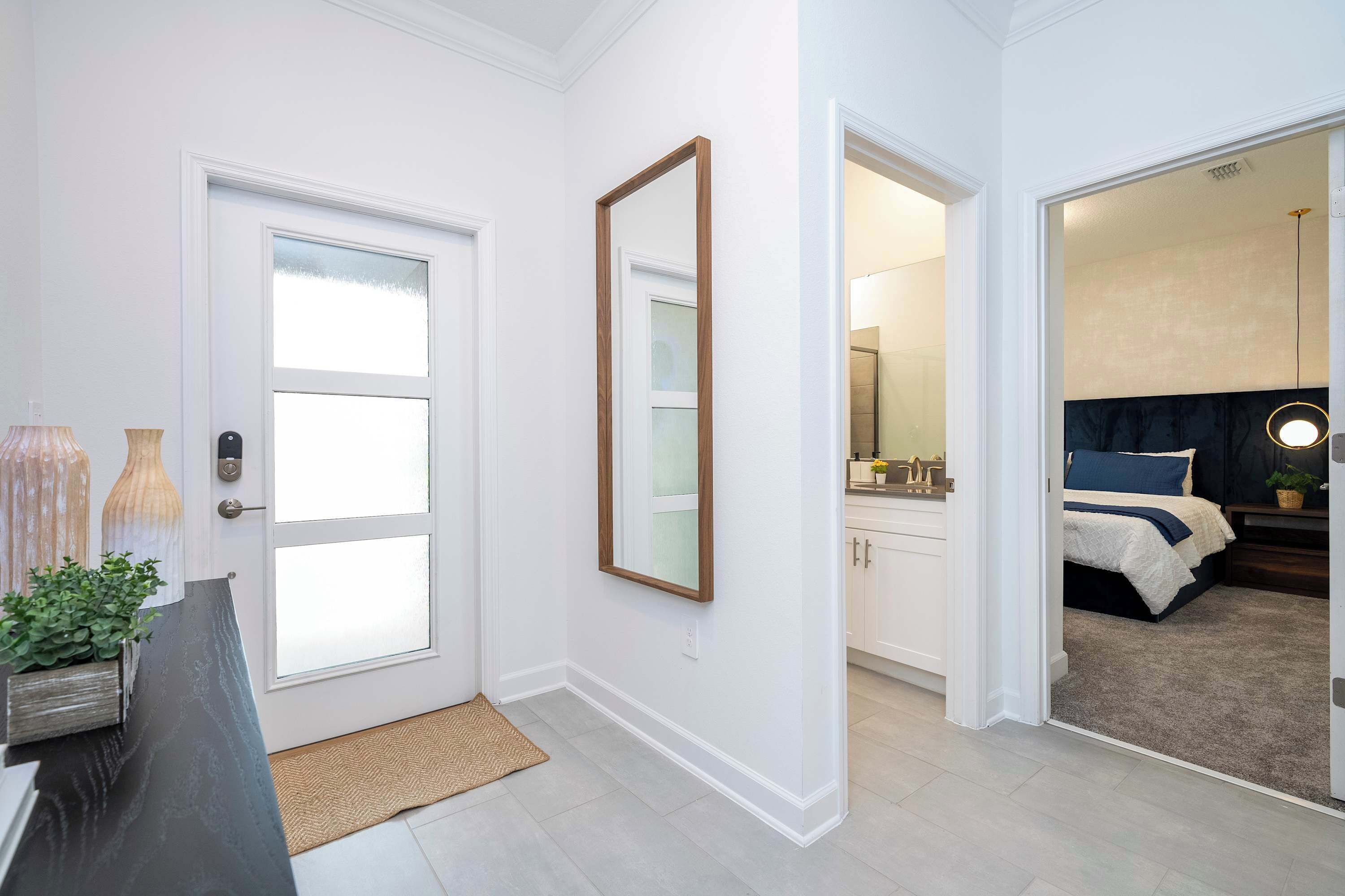 A modern interior with a door, a mirror, a small plant, and a bed in the adjacent room.