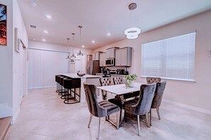 A modern kitchen with a central island, bar stools, and a dining table with chairs. - Private Pool & Game Room Family Retreat at Windsor Cay (Clermont)
