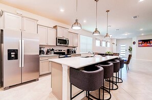 A modern kitchen with a central island, stainless steel appliances, pendant lighting, and bar stools. - Private Pool & Game Room Family Retreat at Windsor Cay (Clermont)
