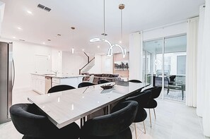 Eine moderne Küche mit einer zentralen Kochinsel, ein Essbereich mit einem langen Tisch und Stühlen sowie eine Treppe, die zu einer oberen Ebene führt.