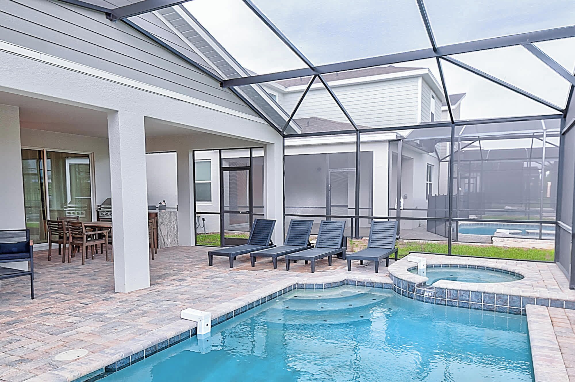 A covered outdoor swimming pool area with lounge chairs and a hot tub.