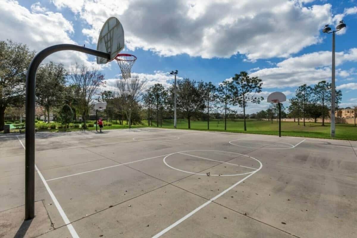 Ein Basketballplatz im Freien mit Korb, blauem Himmel und Bäumen im Hintergrund.
