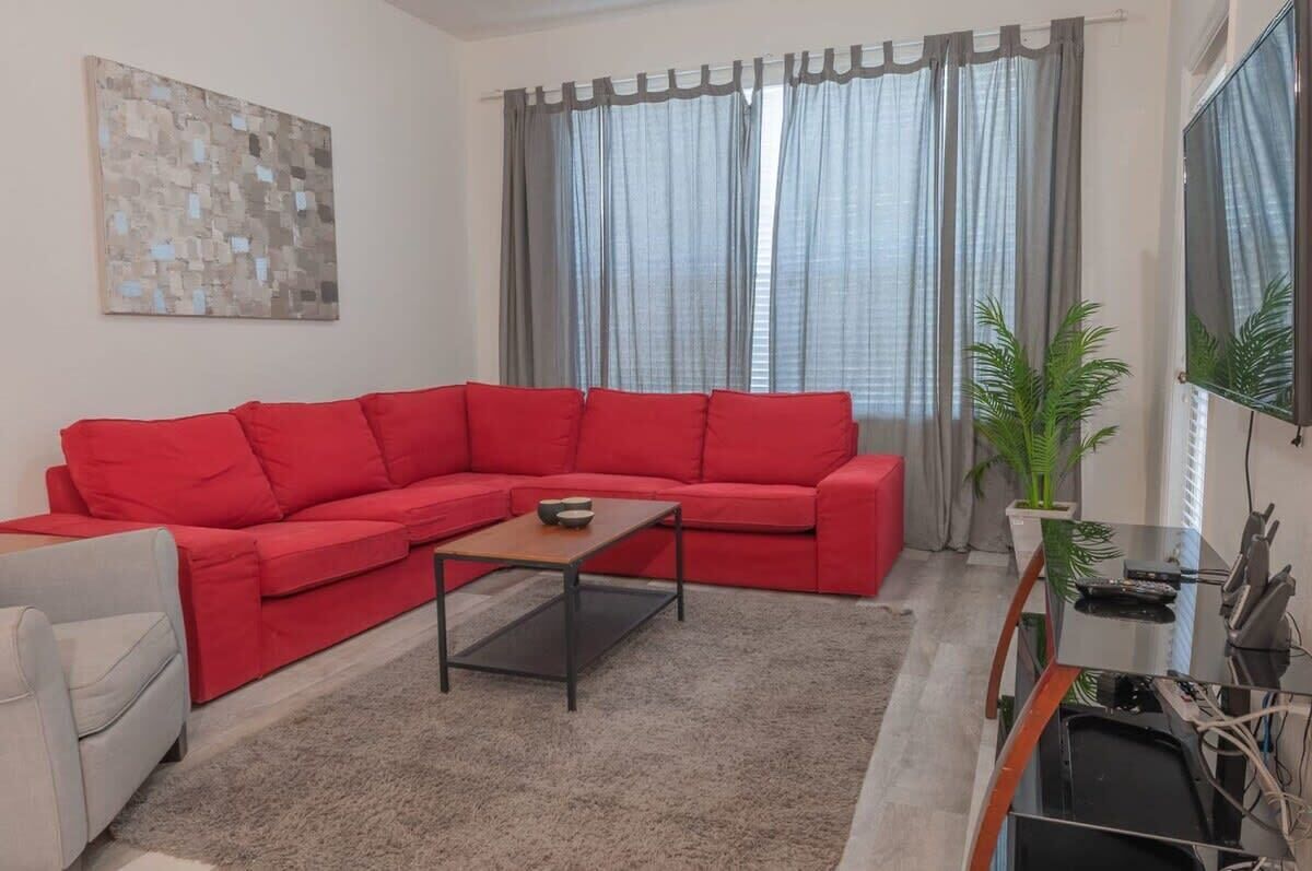 Ein Wohnzimmer mit einem roten Sofa, einem Couchtisch, einem Fernseher und einer Pflanze.