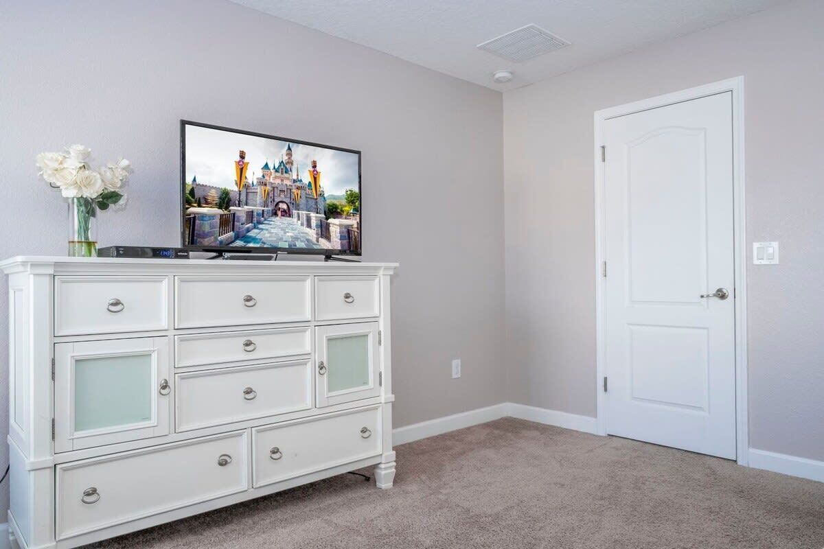 Een kamer met een witte dressoir, een televisie waarop een kasteel te zien is, en een witte deur.