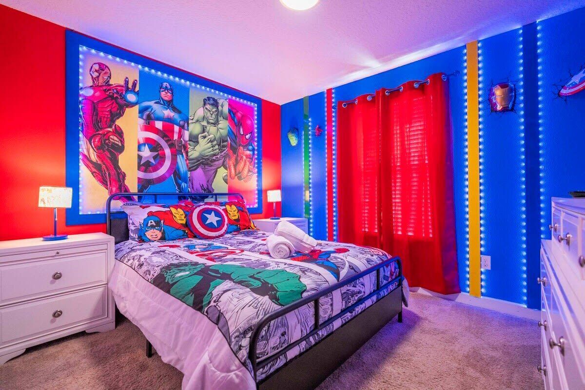A bedroom with a bed, a nightstand, a dresser, a red curtain, and a wall with comic book characters.