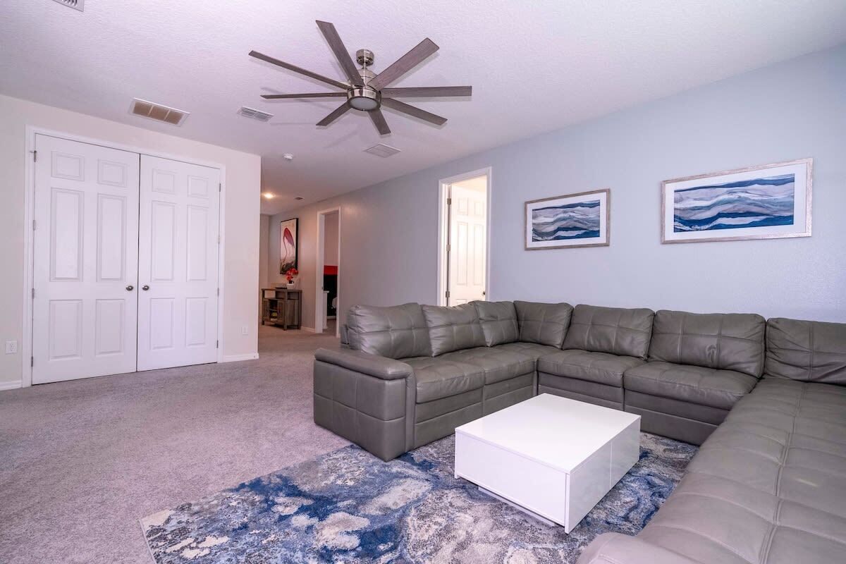 A living room with a sectional sofa, a white coffee table, a ceiling fan, and two framed artworks on the wall.