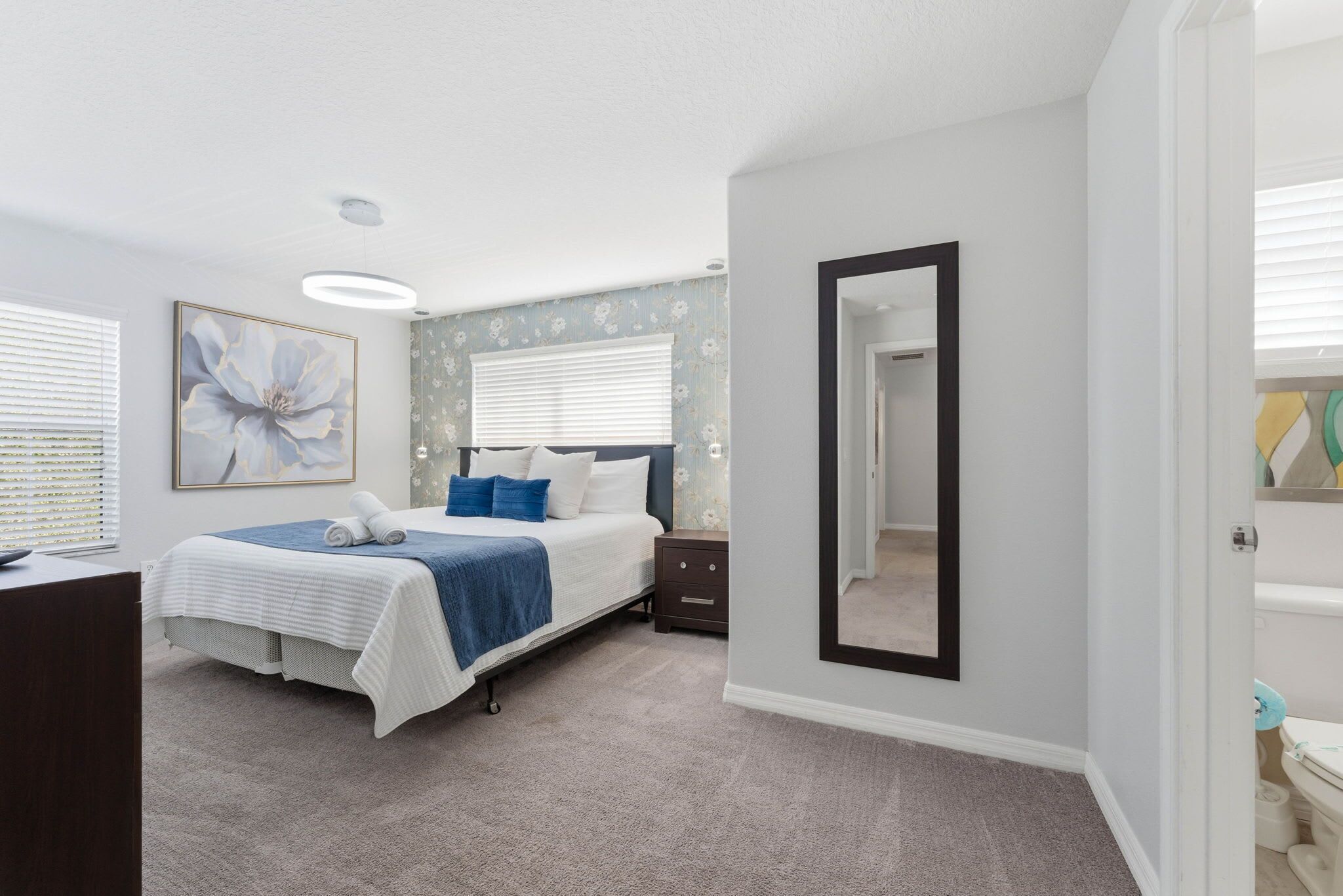 A bedroom with a bed, a nightstand, a mirror, and a window with blinds.