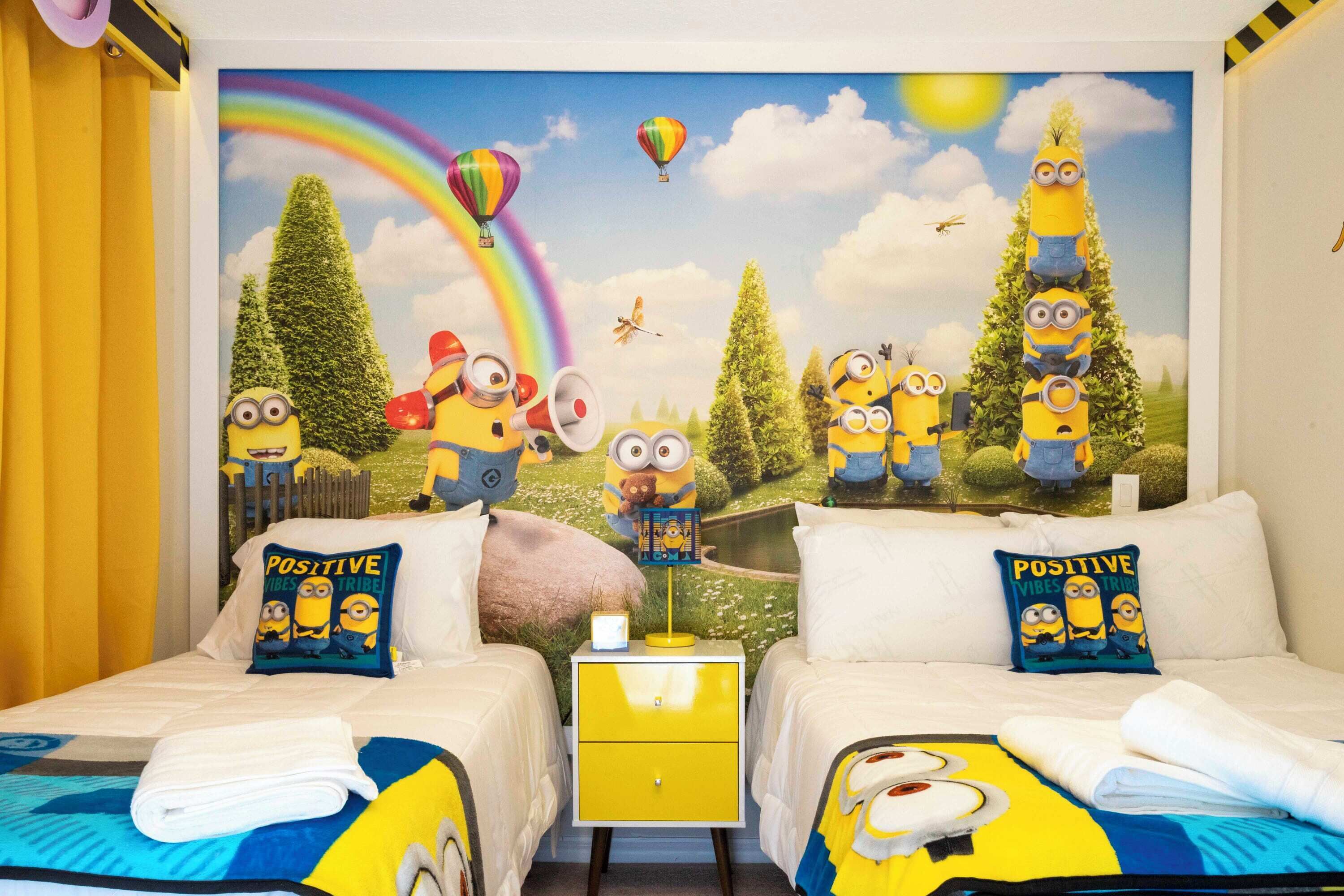Une chambre avec deux lits, une table de chevet et une fresque murale représentant des personnages de dessins animés et un arc-en-ciel.